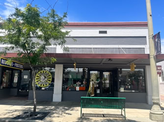 Front view of a vintage record and poster store in Downtown Upland, California, with colorful signage, storefront displays, and a green bench outside.  