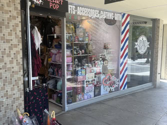 Exterior of Heart Pop store in Upland, California. The storefront has a display window filled with plush toys, bags, and accessories. A neon sign above the entrance reads “Heart Pop.” A bucket of colorful umbrellas is placed outside near the door.